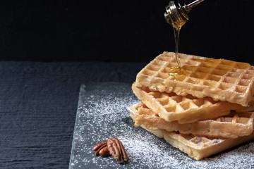 sweet tasty Belgian waffles close-up, sprinkled with powdered sugar, pecans, topped with honey