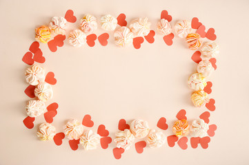 Arrangement for Valentine's Day of pink meringues and red paper hearts. Objects enclose a vertical frame. Free space to place text. Pink background. Close-up.