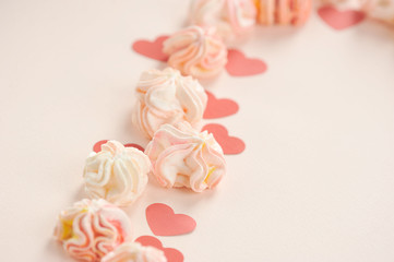 Composition to the Valentine's Day of pink meringues and red paper hearts. Pink background. Free space to place text. Close-up. Macro shooting.