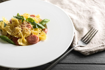 Plate with tasty macaroni and sausages on table