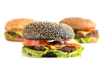 Big black burger on a white background. Beef patty burger, cheddar cheese, lettuce, bacon, pickled cucumber, tomato and balsamic burger burger. In the background are two burgers.