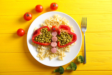 Plate with vegetables, pasta and sausages for child on color wooden table