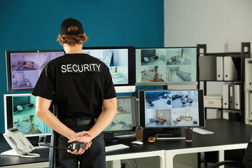 Security guard with portable radio transmitter monitoring modern CCTV cameras in surveillance room