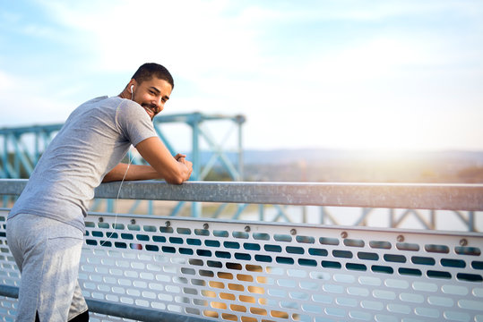 Young sporty man on the bridge having a break. Sportsman enjoying beautiful view. 