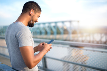 Young attractive sporty man using phone and smiling on the bridge.