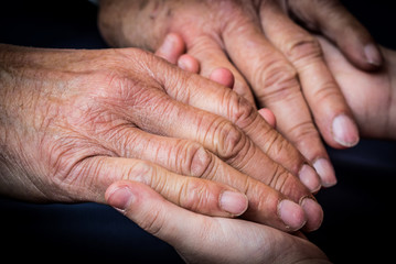 Fototapeta premium Old male and young female hands on a dark background