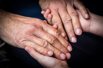 Old male and young female hands on a dark background