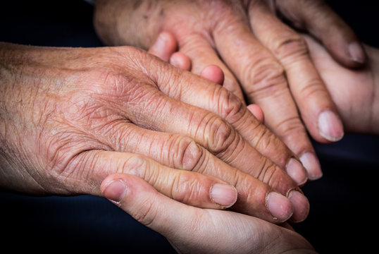 Old male and young female hands on a dark background