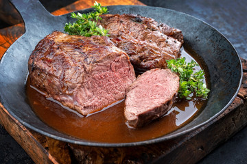 Traditional barbecue aged saddle of venison with herbs game sauce as closeup in a wrought iron skillet