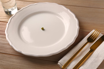 Plate with small peas and cutlery on wooden table. Diet concept