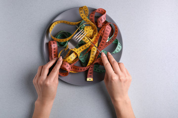 Female hands with plate, cutlery and measuring tapes on light background. Diet concept