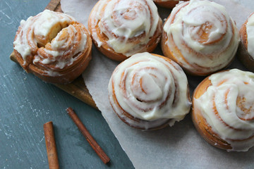 Beautiful fresh cinnamon rolls close-up on wooden grunge texture table. Fragrant homemade cakes, Cinnabon. A Cup of tea on a white saucer, cinnamon sticks. Delicious Breakfast buffet.