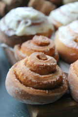 Beautiful fresh cinnamon rolls close-up on wooden grunge texture table. Fragrant homemade cakes, Cinnabon. A Cup of tea on a white saucer, cinnamon sticks. Delicious Breakfast buffet.