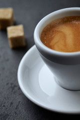 Cup of coffee and two brown sugar cubes on black stone background. Close up. 
