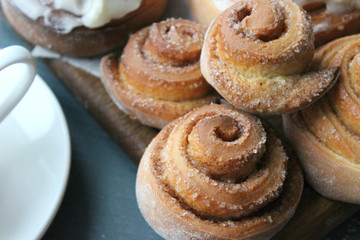 Beautiful fresh cinnamon rolls close-up on wooden grunge texture table. Fragrant homemade cakes, Cinnabon. A Cup of tea on a white saucer, cinnamon sticks. Delicious Breakfast buffet.