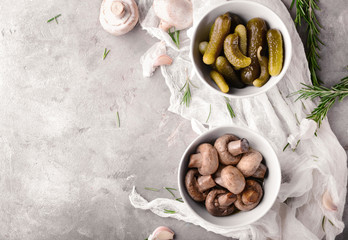Bowls with tasty fermented mushrooms and cucumbers on grey table