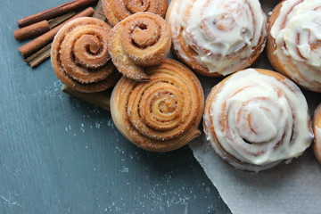 Beautiful fresh cinnamon rolls close-up on wooden grunge texture table. Fragrant homemade cakes, Cinnabon. A Cup of tea on a white saucer, cinnamon sticks. Delicious Breakfast buffet.