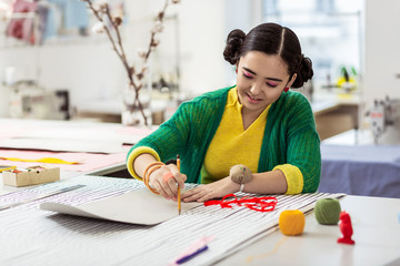 Cute brunette asian dressmaker with pink eyeshadows drawing a picture