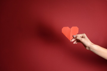 Female hand with origami heart on color background
