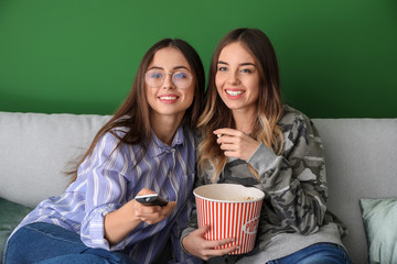 Young women eating popcorn while watching TV at home