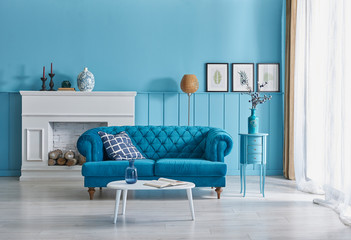 Blue room, blue sofa and pillow, vase of plant with white fireplace, orange lamp and frame decoration.
