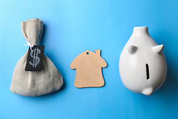 Piggy bank, figure of house and bag with money on color background. Mortgage concept