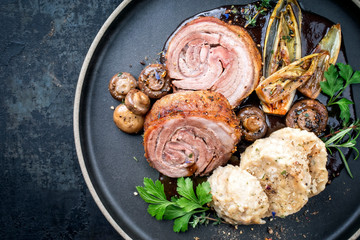 Traditional rolled boar roast with dumpling, fried vegetable and mushroom as top view on a modern design plate with game red wine sauce with copy space left