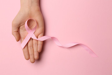 Female hand with pink ribbon on color background. Breast cancer awareness concept
