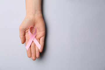 Female hand with pink ribbon on light background. Breast cancer awareness concept