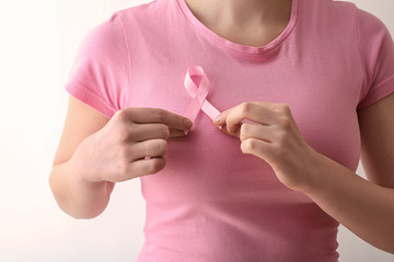 Woman with pink ribbon on white background, closeup. Breast cancer awareness concept