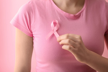 Woman with pink ribbon on color background, closeup. Breast cancer awareness concept
