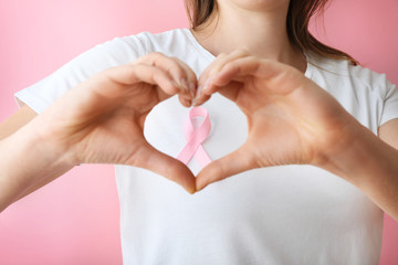 Woman with pink ribbon making heart with her hands, closeup. Breast cancer awareness concept
