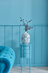 Wooden blue wall background, blue vase of plant and sofa arm detail.