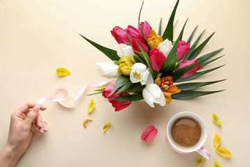 Female hand, beautiful flowers and cup of coffee on light background