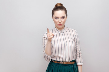 Serious beautiful young woman in striped shirt and green skirt, makeup and collected ban hairstyle,...