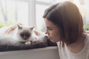 Woman petting her cat next to a window
