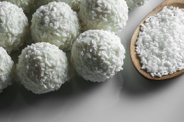 White chocolate ball candy with coconut topping and coconuts in spoon on white plate. Coconuts pastry concept