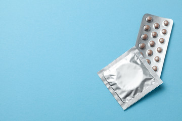 Birth control pills and condom in package on blue background. The concept of choosing method of contraception, birth control pills or condom. Copy space for text