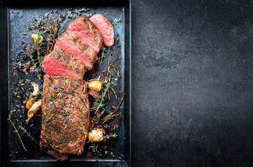 Traditional barbecue aged venison backstrap roast with herbs as top view on a rustic metal sheet...