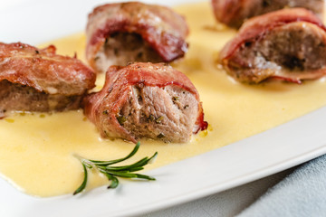 Baked pork tenderloin wrapped in bacon and served in a cheese sauce with rosemary