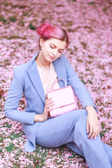 girl with pink hair in a blue stylish suit sitting on a background of pink petals