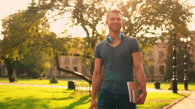 happy guy speaking by cellular on the street smiling cheerful student holding books and notebook in sunlight