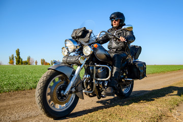 Fototapeta na wymiar Motorcycle Driver Riding Custom Chopper Bike on Autumn Dirt Road in the Green Field. Adventure Concept.