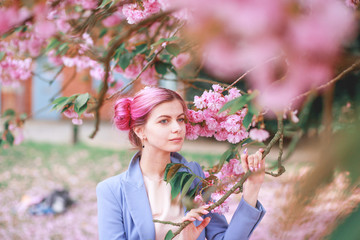 Obraz premium Beautiful girl with pink hair in a fashionable blue pantsuit standing next to colorful flowers.