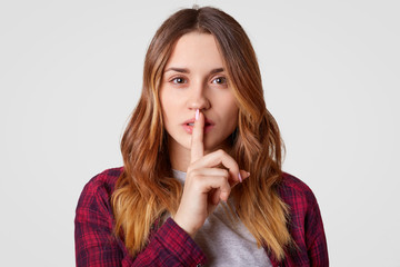 Beautiful tender woman males silence gsture, looks secretly at camera, dressed in casual outfit,...