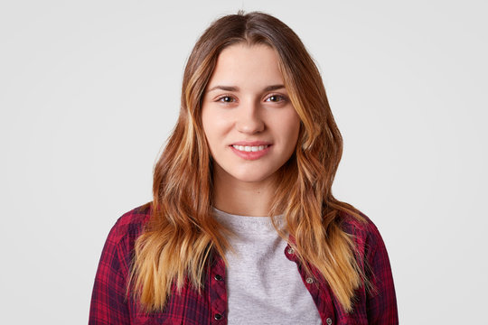 Close up shot of cheerful woman has tender expression, dyed wavy hair, dressed in casual clothes, models over white background. European lady smiles positively, shows white teeth, grins at camera