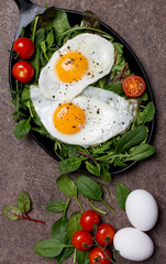 Fried eggs with fresh herbs and cherry tomatoes at pan on brown background