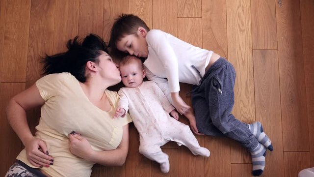 Top view happy family mother with kid son kiss little baby sister lying on floor