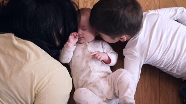 Top view happy family mother with kid son kiss little baby sister lying on floor