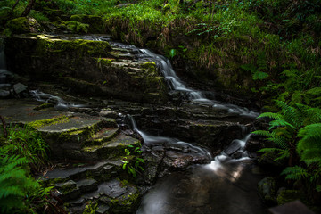 Naklejka na ściany i meble Small Long Exposured Creek With Waterfall In Mystic Forest Near Ullapool In Scotland